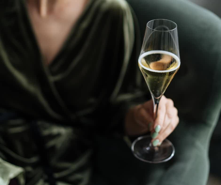 Woman dressed in green and holding up a champagne flute glass
