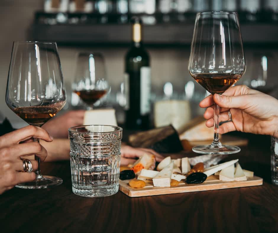 Holding up glasses of wine with a cheese and snack platter