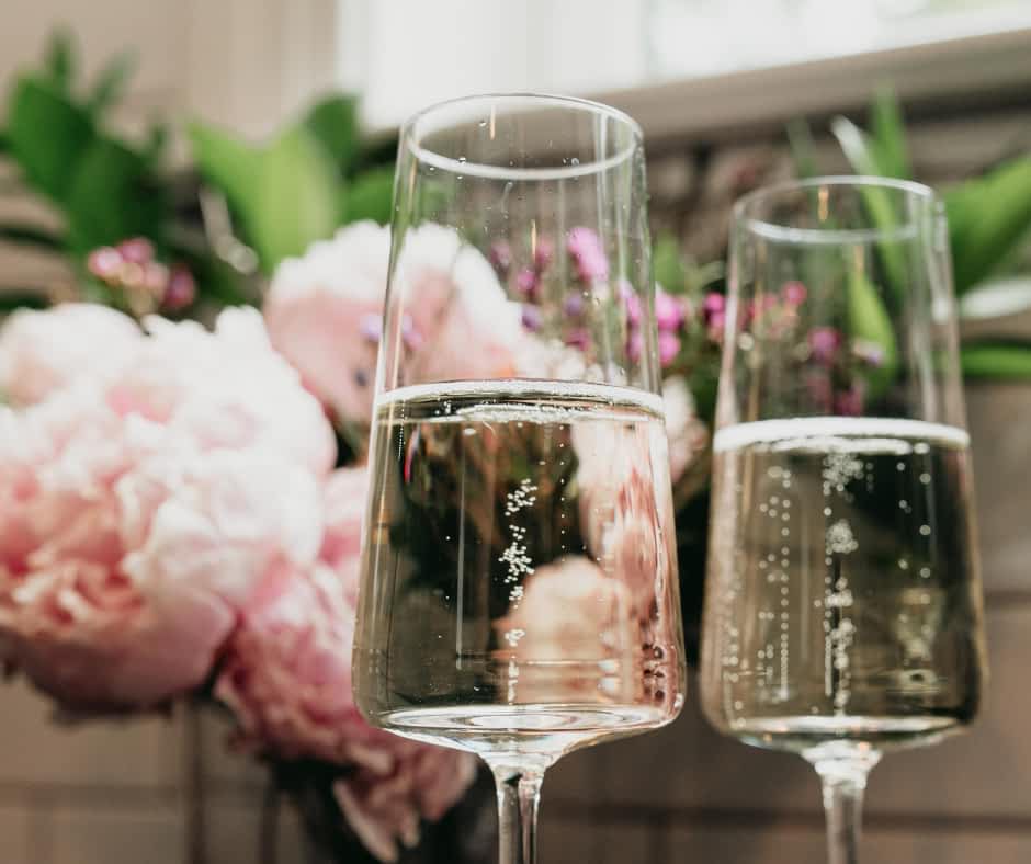 Two glasses of sparkling wine in front of pink flowers.